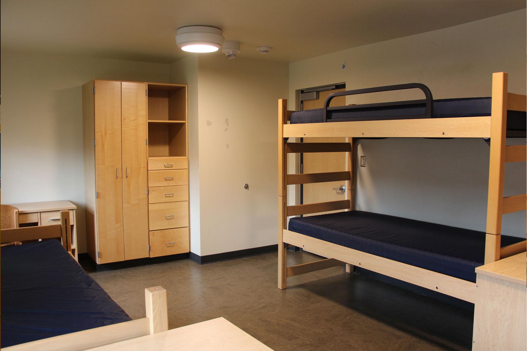 Example of a renovated triple residence hall room, featuring two lofted bunk beds, another bed, built-in storage cabinets, and study desks.