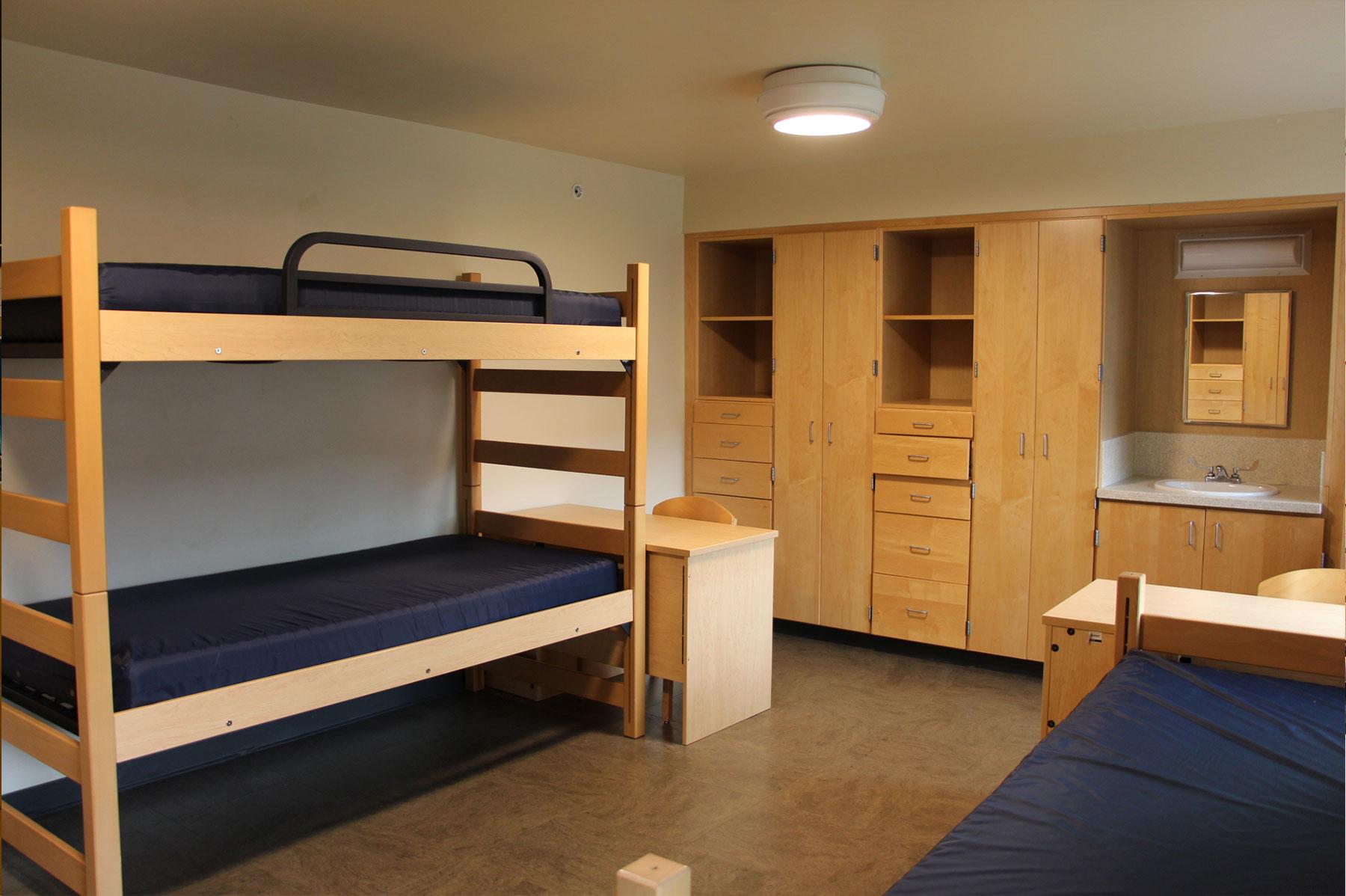 Example of a renovated triple residence hall room, featuring two lofted bunk beds, another bed, built-in storage cabinets, and study desks.