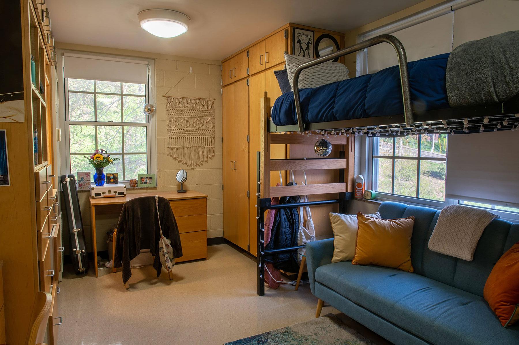 Example of a single room on East Green, featuring a lofted bunk bed with a couch underneath, a desk, and built-in storage cabinets