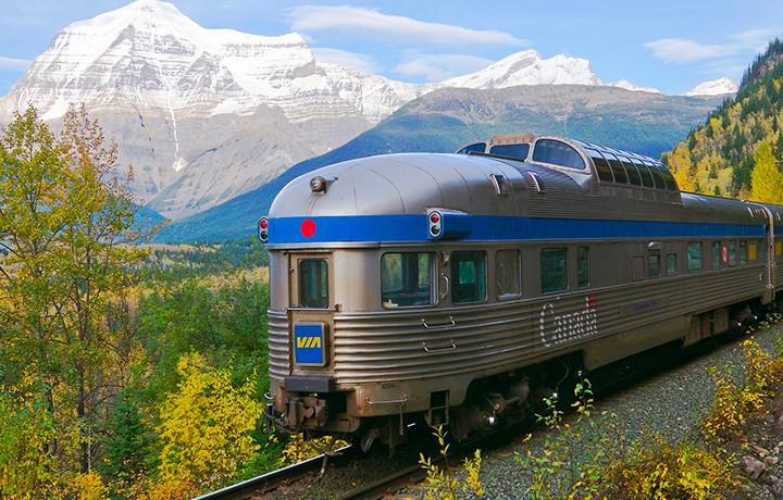Train traveling through wilderness with snowy mountains in the background.