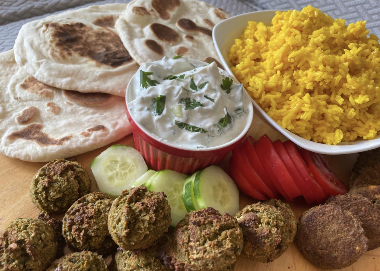 A wooden platter containing naan. tzatziki, falafel, rice and vegetables.