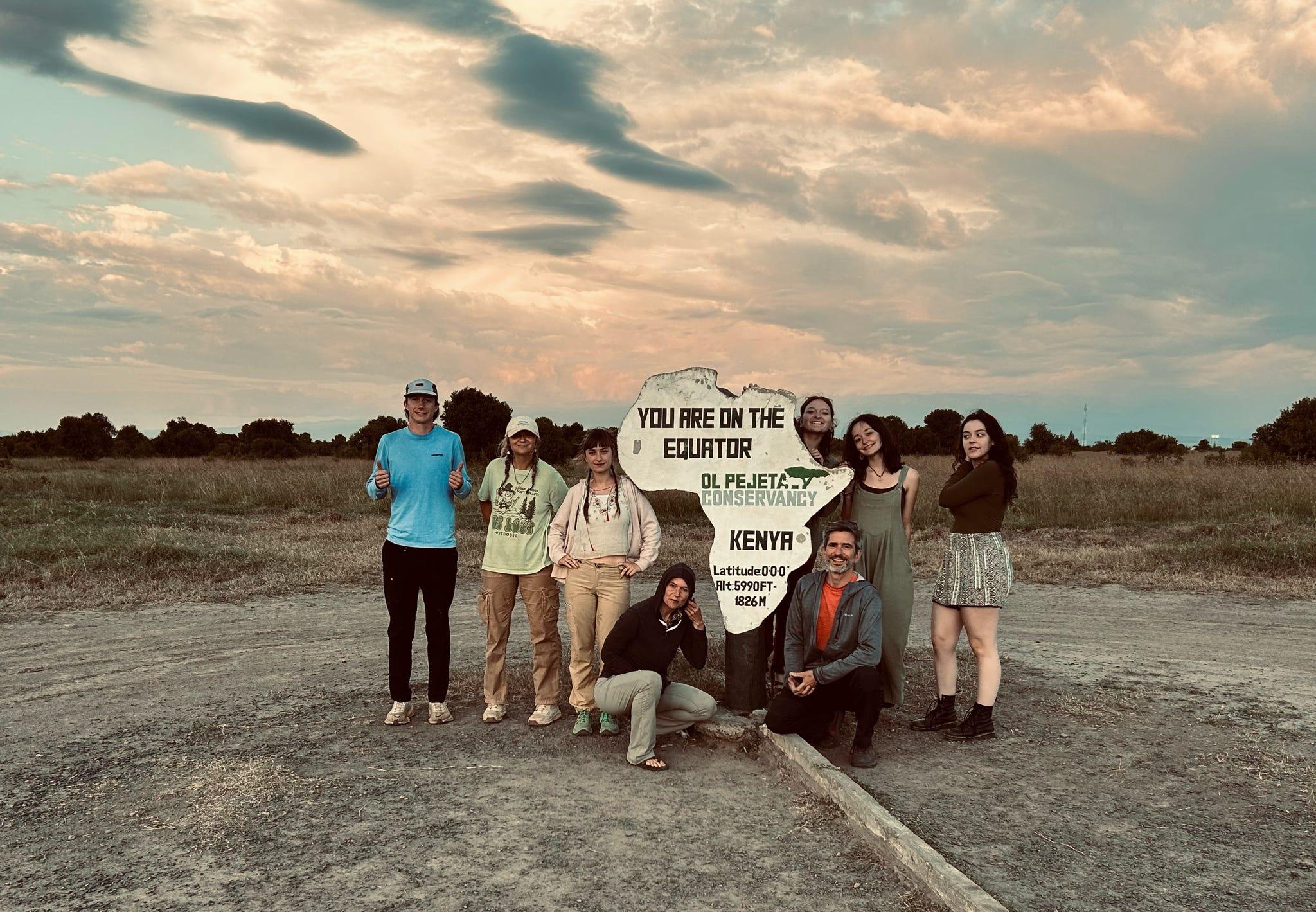Group of students in Kenya in front of sign in the shape of the African continent, background shows a cloudy sunset