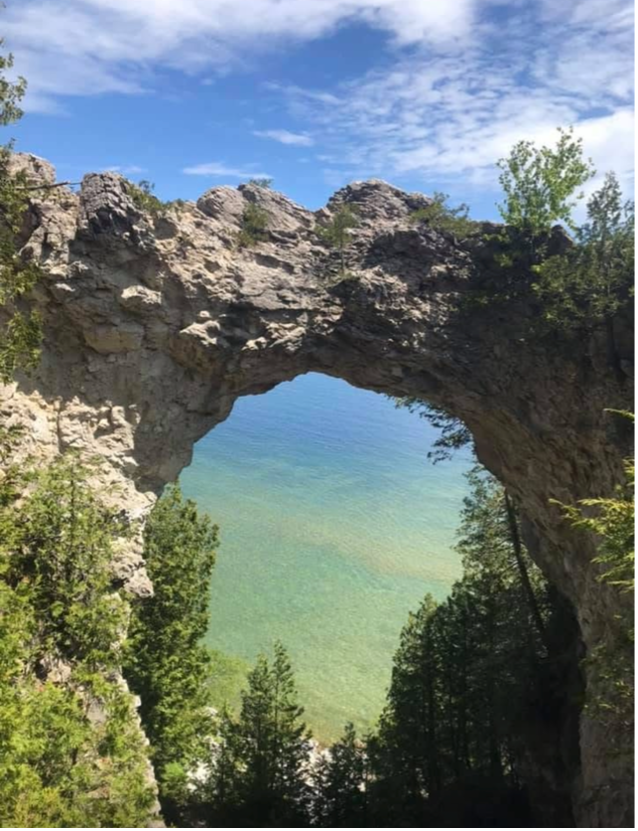 Arch Rock natural bridge on Mackinac Island with blue sky, trees and lake in the background