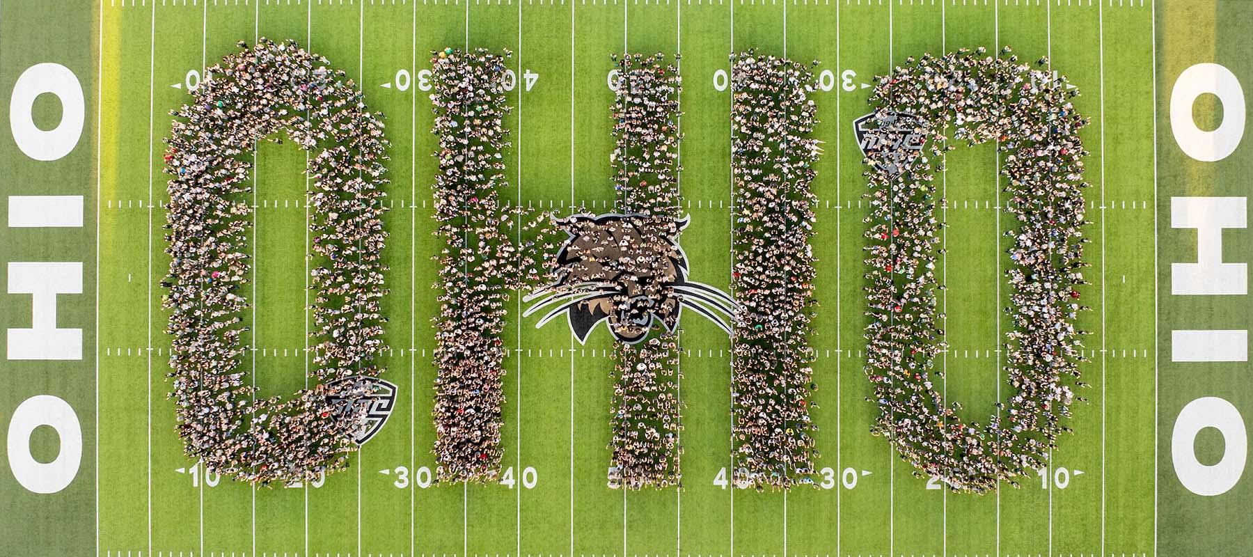 Students stand on a football field in clusters to form the word "OHIO."