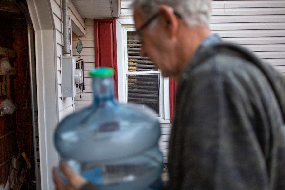 Someone carries a large jug of water into a house