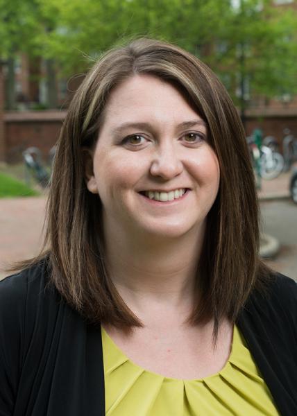 A headshot of a woman with brown hair, wearing a yellow shirt
