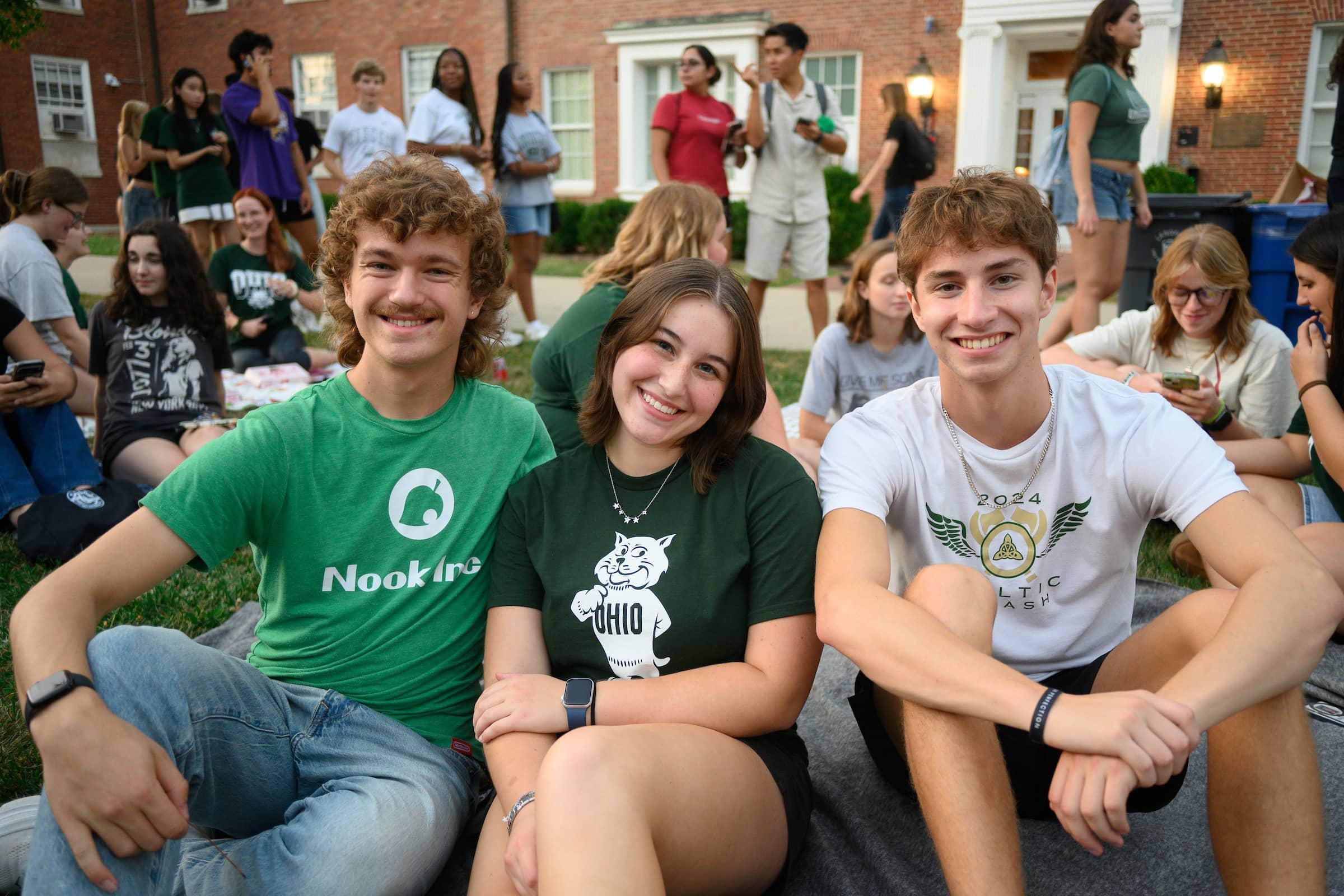 3 students pose sitting on the res hall lawn during the outdoor Welcome Week movie