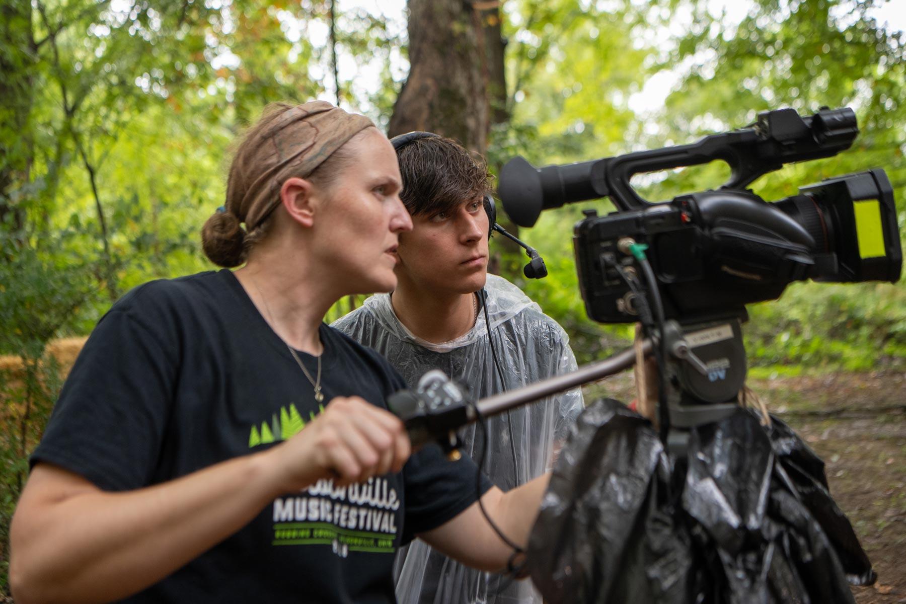 Students look at a video camera while standing in a forest