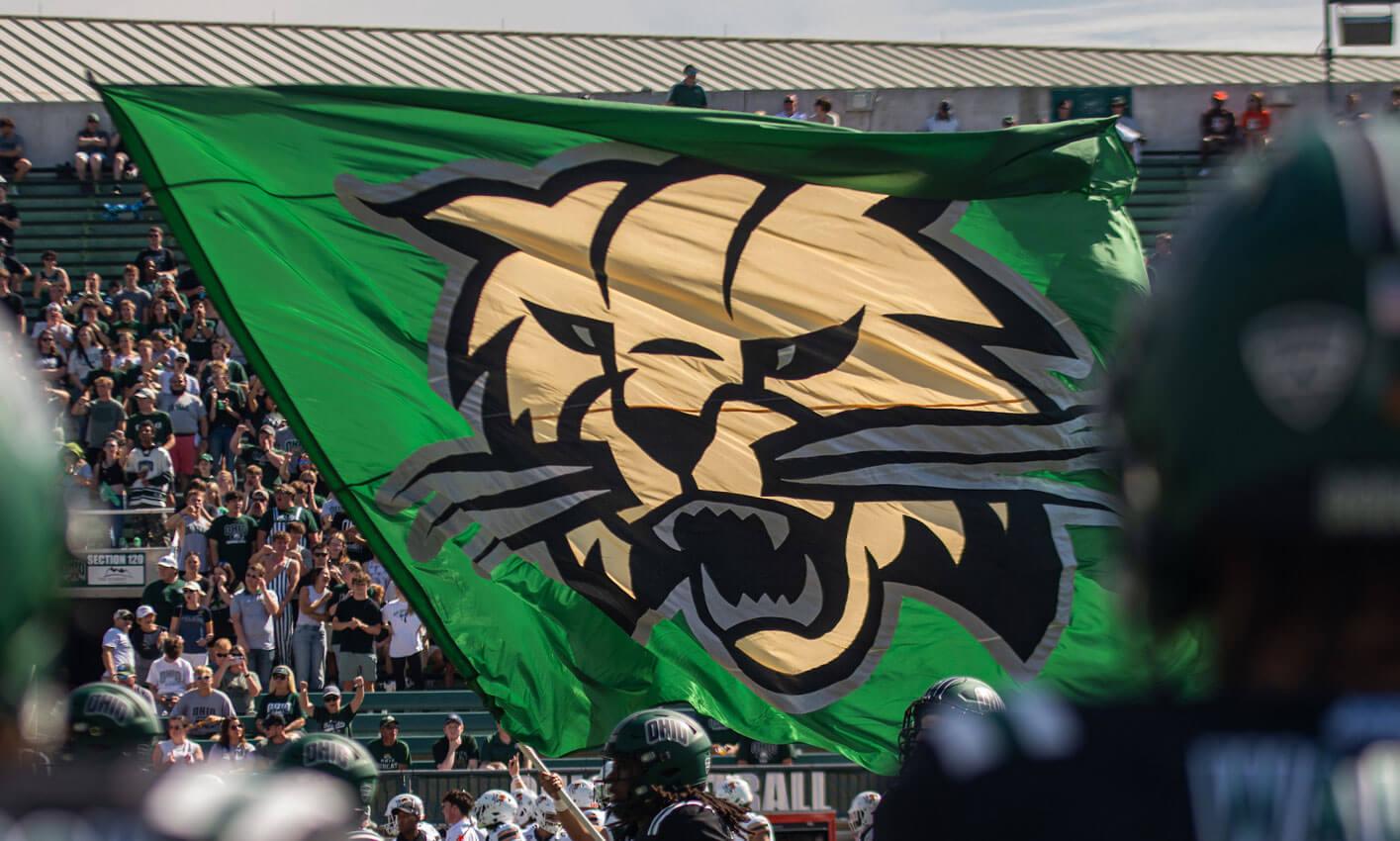Ohio University men's football team runs out on the field carrying the Attack Cat flag.