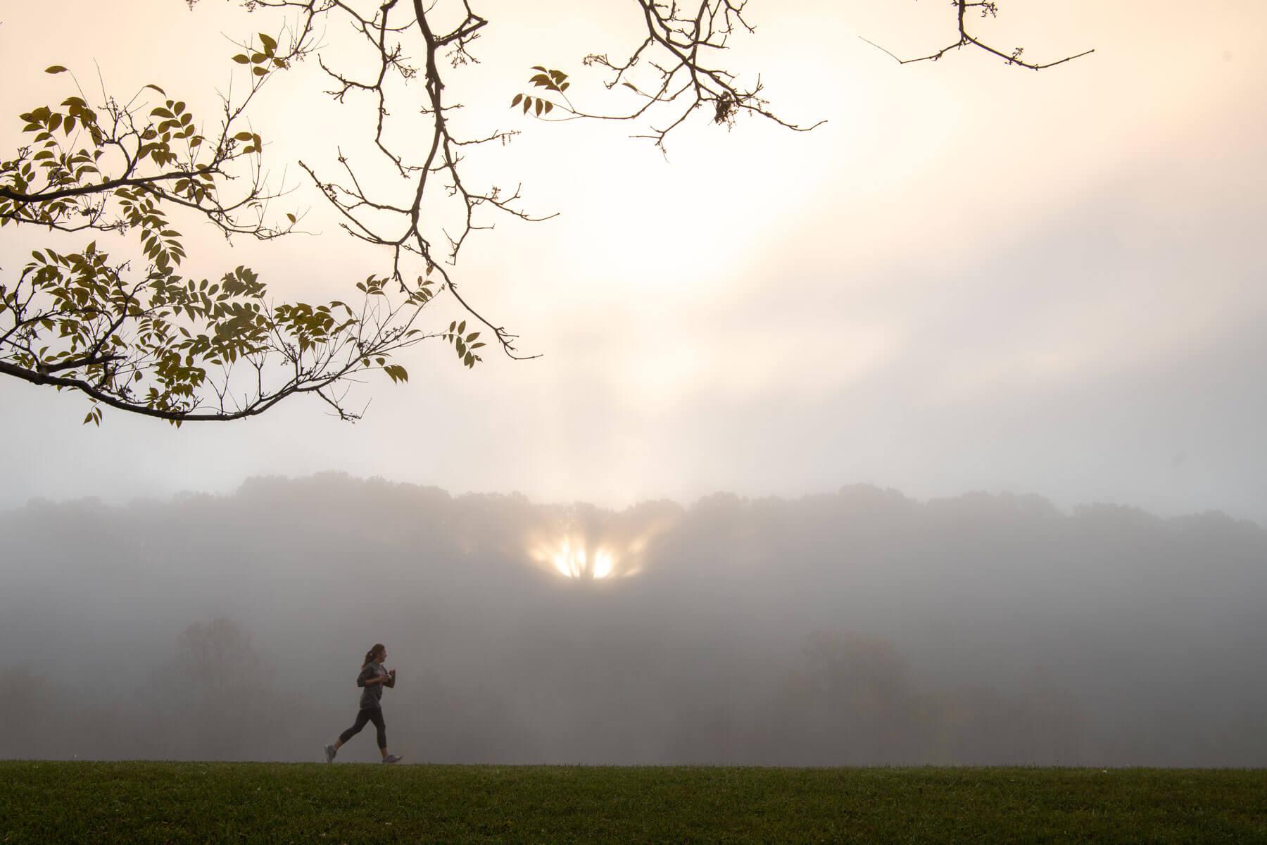 A person runs on the Athens bike path with a sunset peeking through the clouds in the background