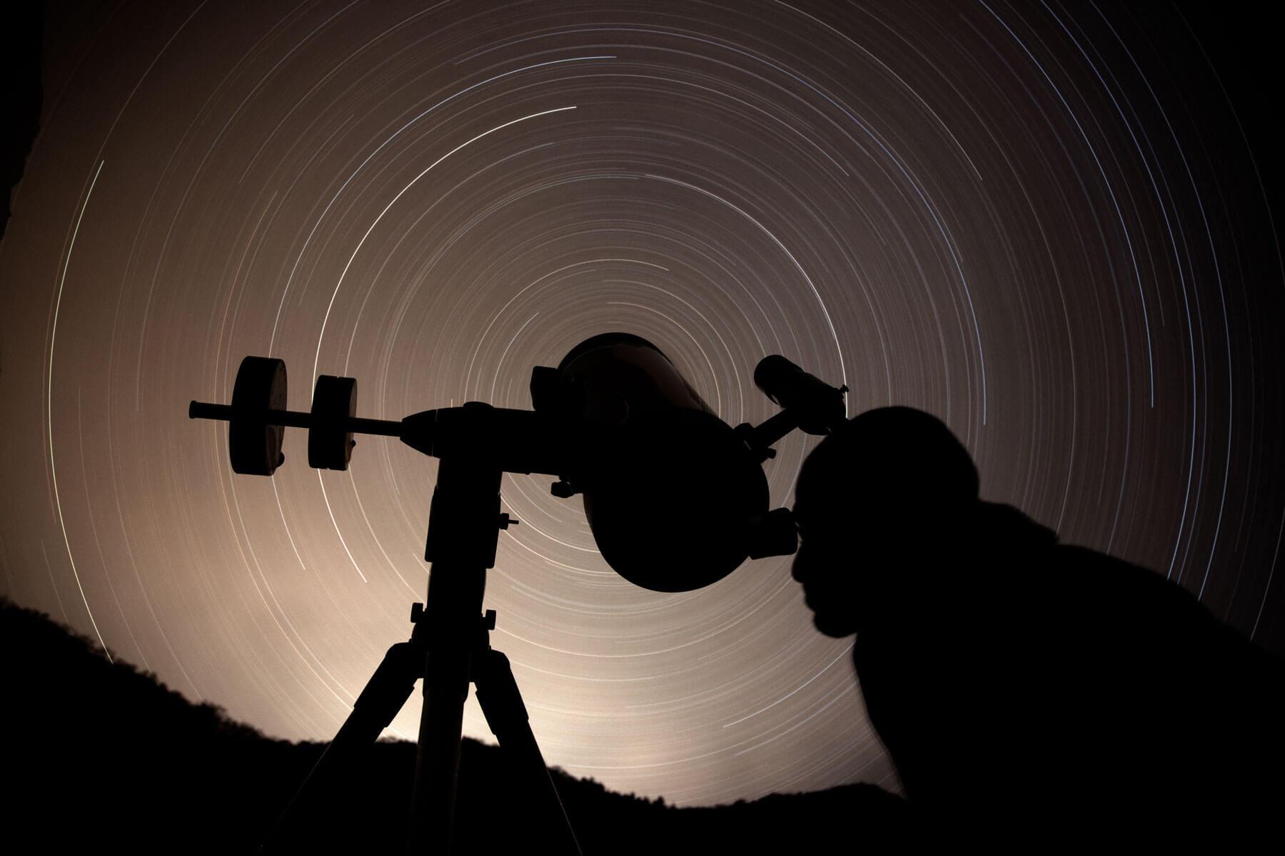 A silhouette of a telescope against a long-exposure blur of a starry sky