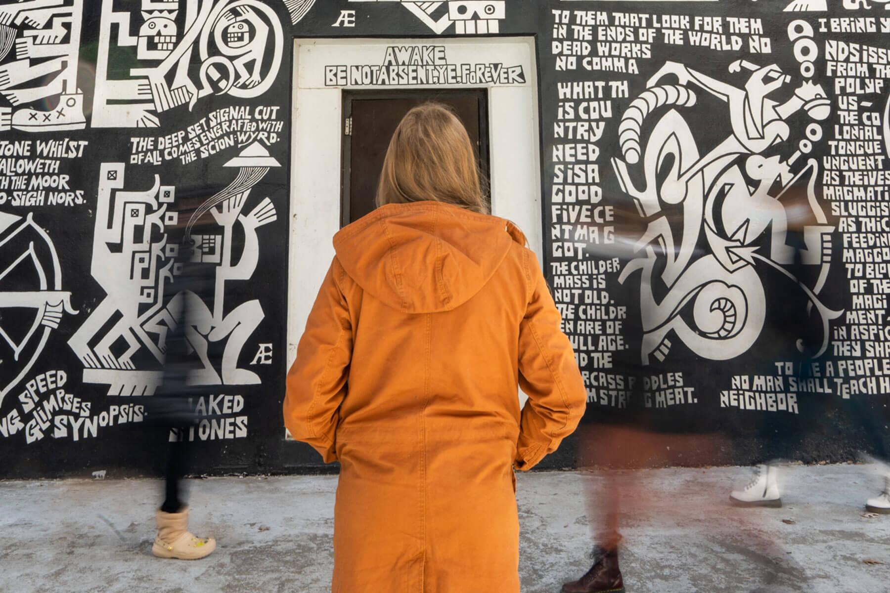 A student in an orange jacket looks at the Æthelred Eldridge mural in Seigfred Hall