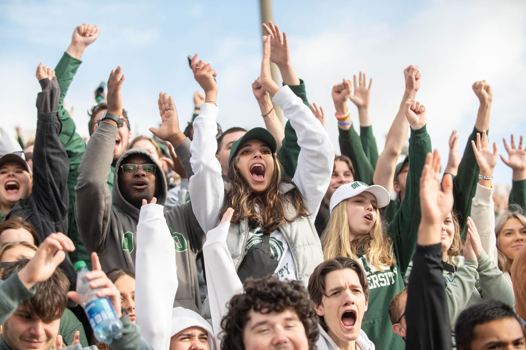 A crowd of OHIO Students cheer with their hands raised in the air