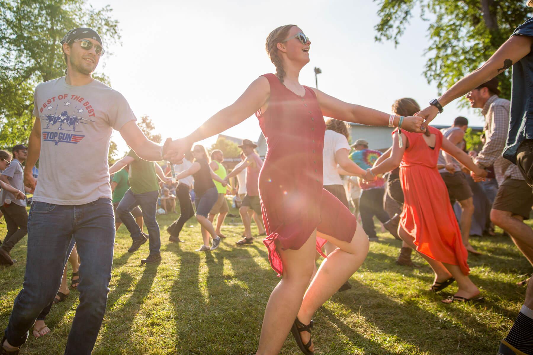 A group of people holding hands and dancing during a performance at Nelsonville Music Festival