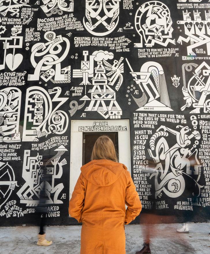 A student in an orange jacket looks at the Æthelred Eldridge mural in Seigfred Hall