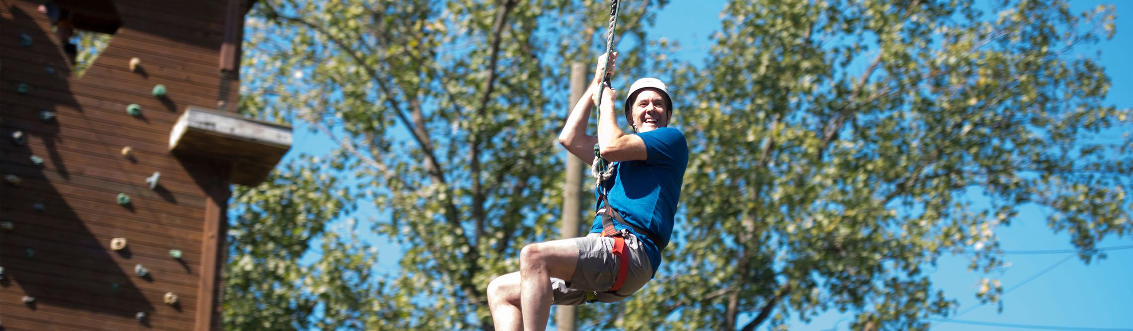 man having fun sliding down on the zipline in challenge course