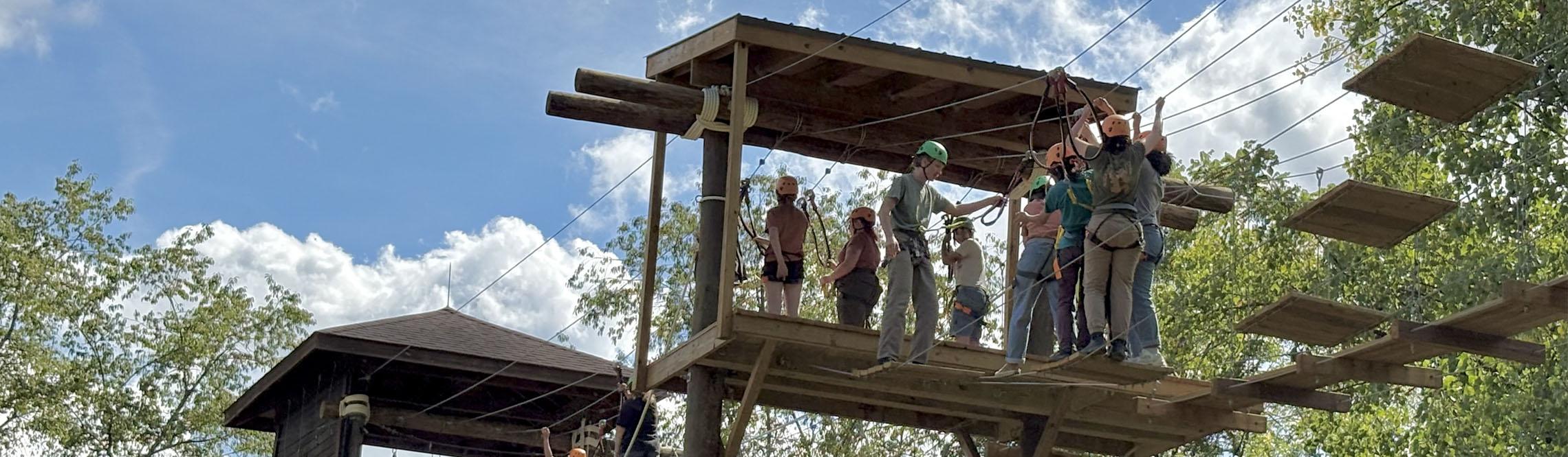 group of teammates prepare to do the odyssey course on top of a high structure
