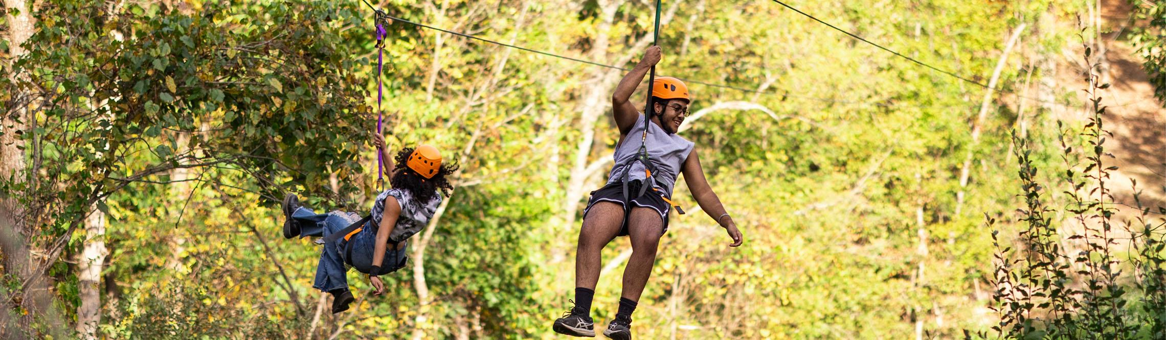 two friends smile while they cruise down the zipline with beautiful green background