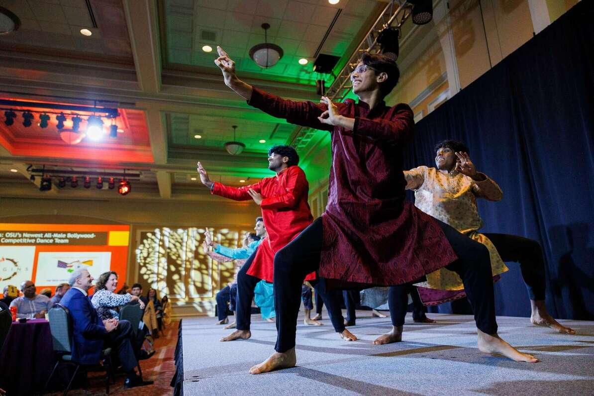 Three OSU Origins dancers stand front and center on stage performing traditional dance
