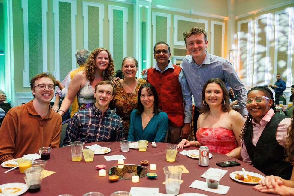 HCOM together sitting and standing around a table smiling
