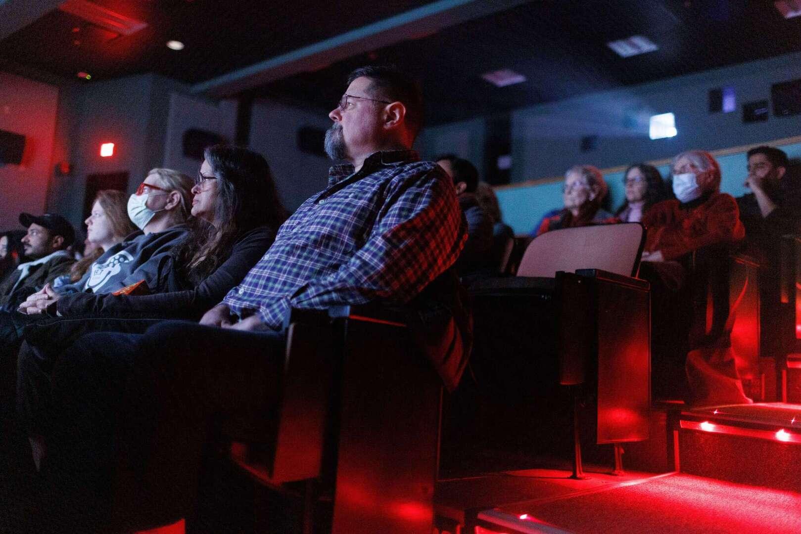 Low angle of movie seating with red LED lights lining rows of seats. Five people sit watching a movie.
