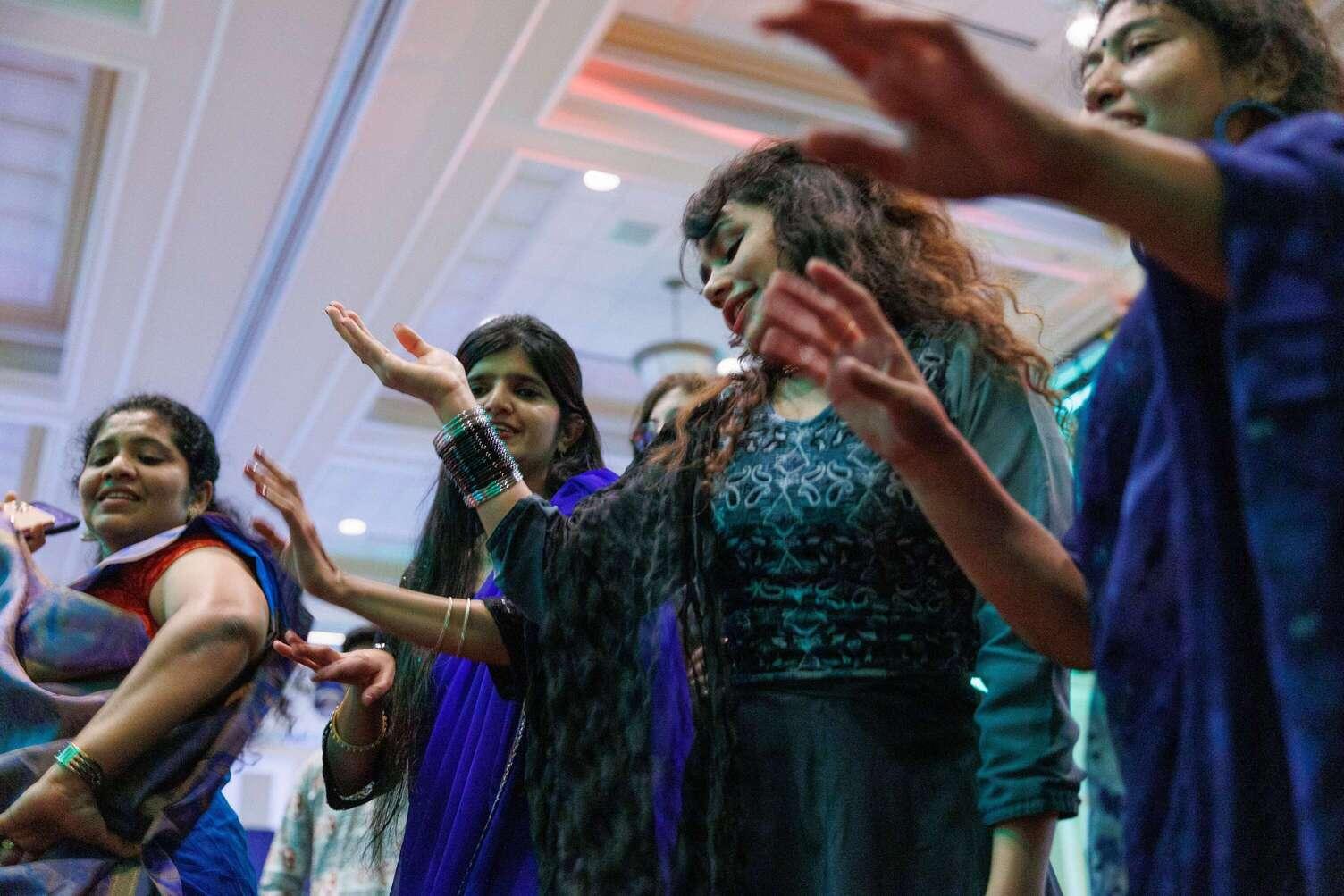 Four members of Friends of India stand clapping wearing blue and green traditional clothing