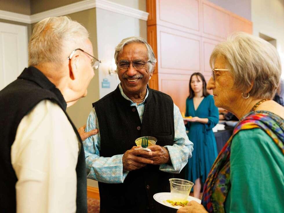 Dr. Raj and Dr. Ashok stand next to each other talking with a woman standing to their left holding a plate