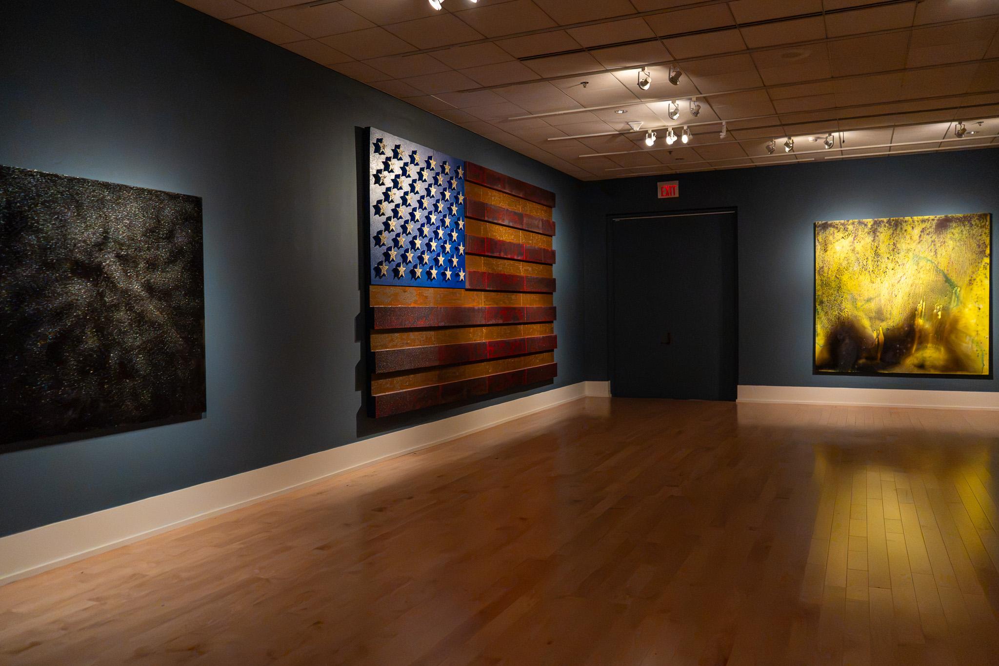 Gallery view of two abstract paintings and American flag