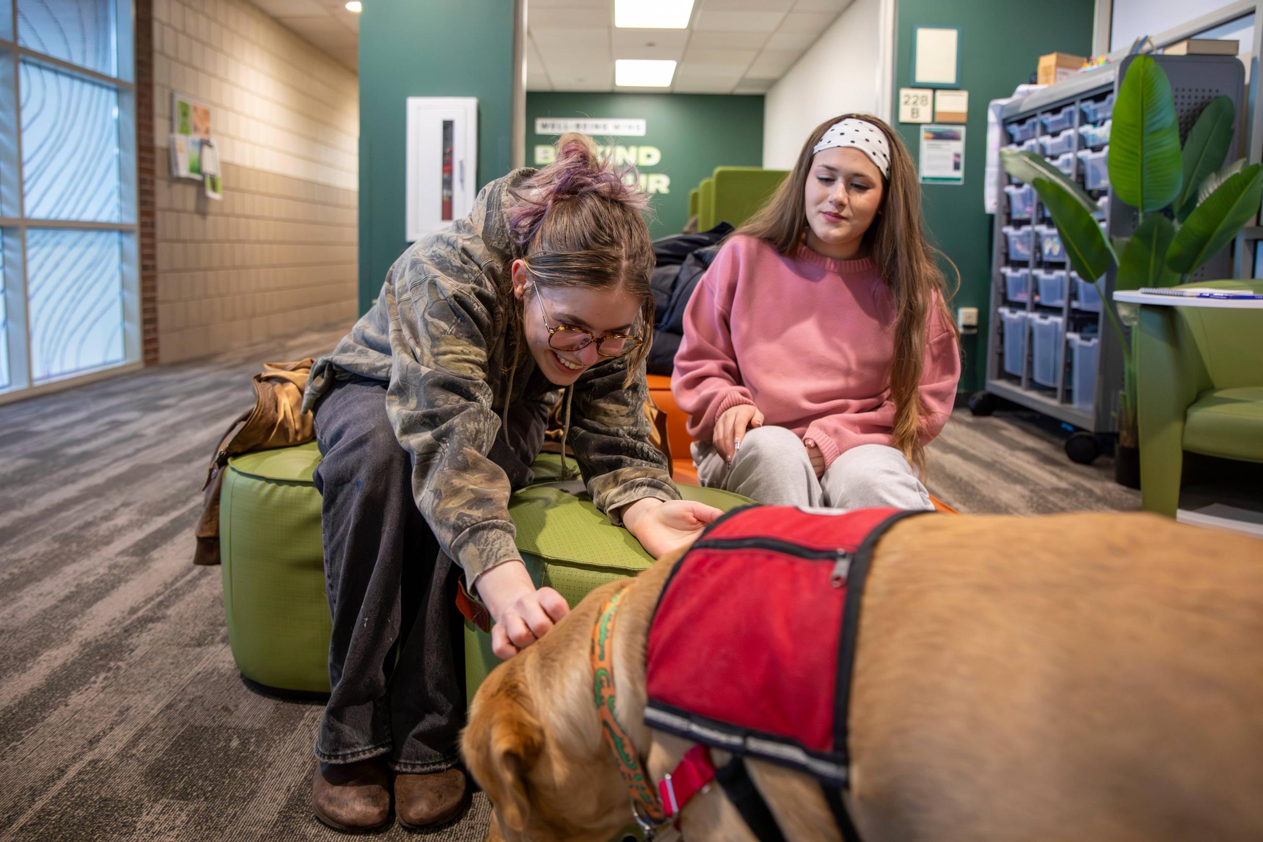 two girls sitting on a couch one of them petting a golden retriever dog happy and smiling