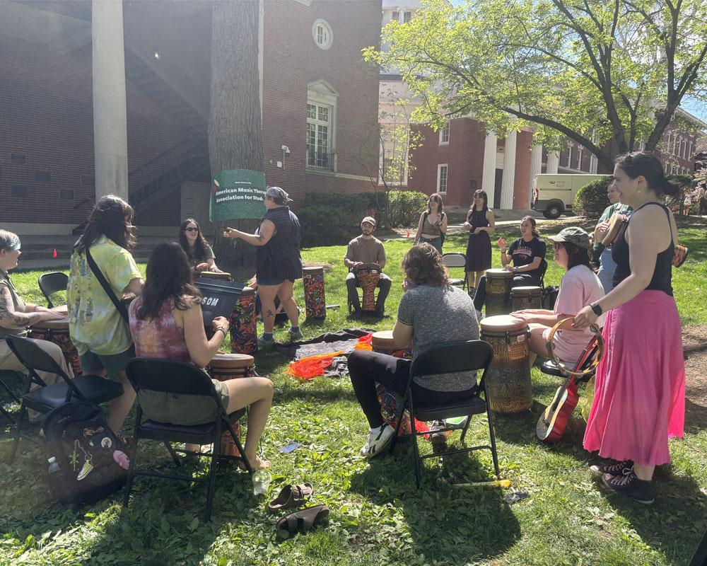 group of students play the drum in a circle on college green