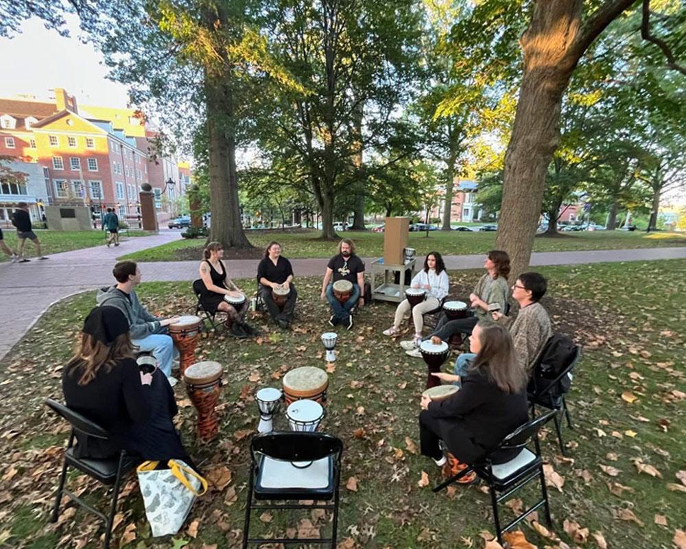 group of students sit in a circle playing the drum