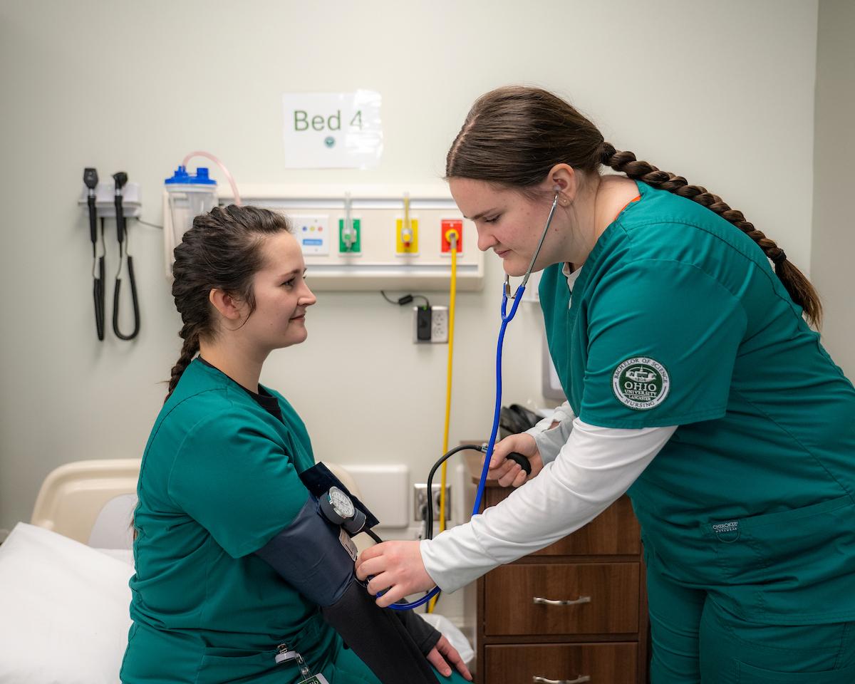 Two Ohio University nursing students practice an exam on each other.