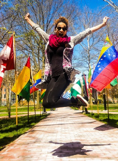 International Week participant jumping in front of a row of international flags.