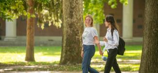 Two students walk across College Green while talking.