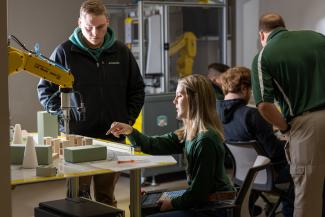 Two students work on automated technology in a lab with other students and a professor