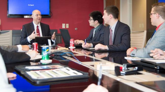 Students sit around a table with a business professional