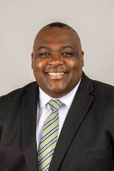 Dr McNeal showed from waist up in a black suit, white shirt and green tie