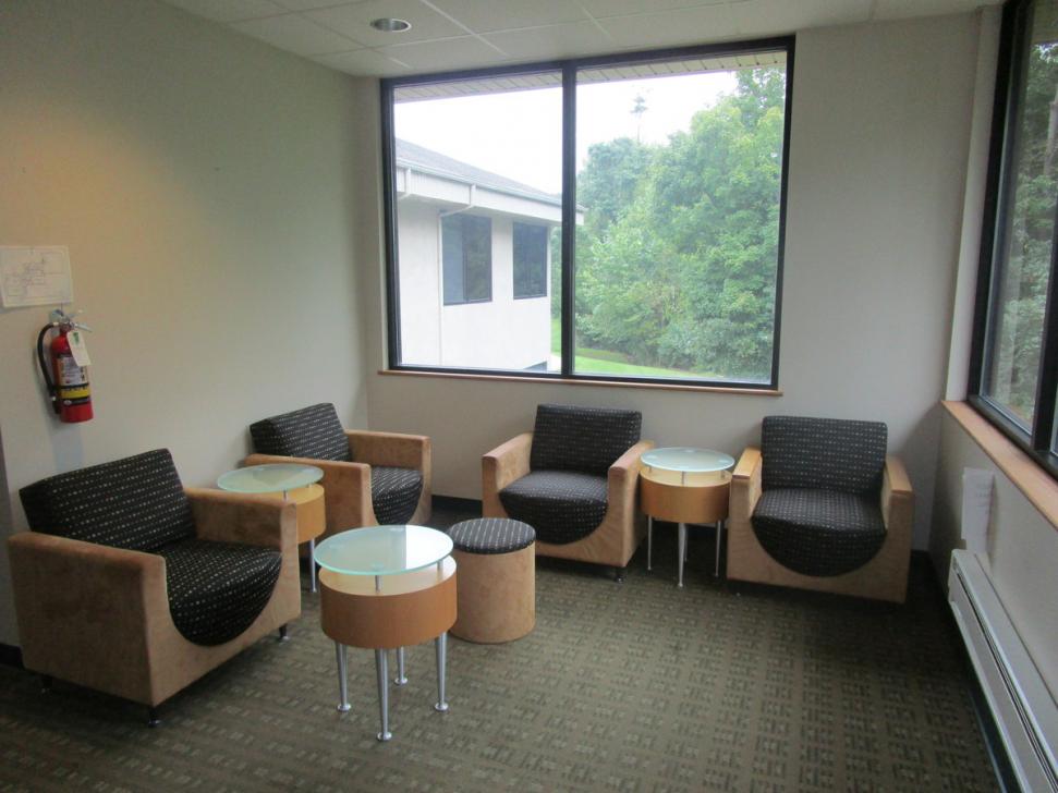 Waiting room with windows on two walls, four modern-design cushioned chairs and some small coffee tables