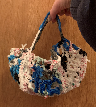 A bag crocheted out of disposable plastic bags. The bags are all different colors and the bag expands when something is placed into it.