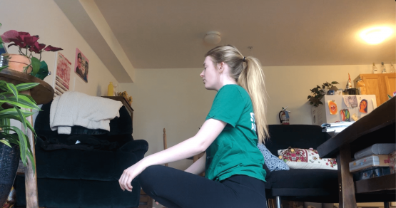 Taylor sits on her floor, cross legged and hands on her knees. She is meditating in her living room while watching Yoga with Adriene.