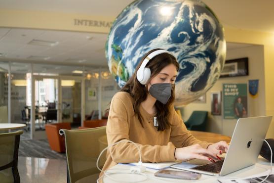 An Ohio University student works on her laptop while wearing a KN95 mask.
