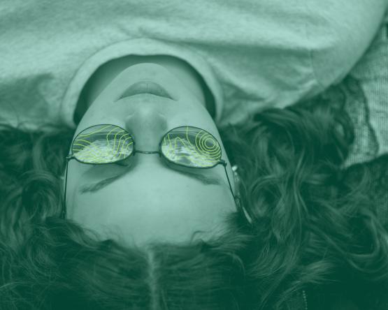 Close-up of a student laying down with topography lines reflected in their sunglasses