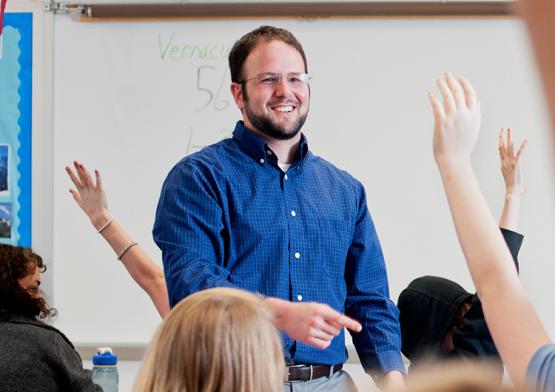 A man in a blue shirt teaching a class while students raise their hands
