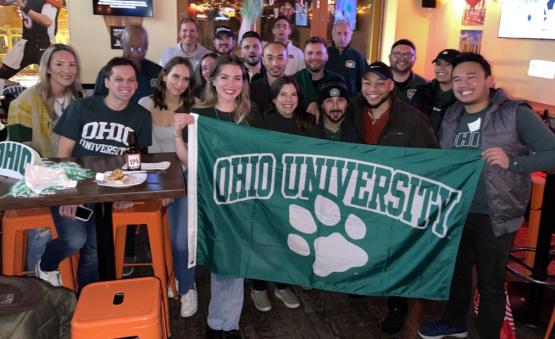 Group of Bobcats holding up green Ohio University flag with paw print.