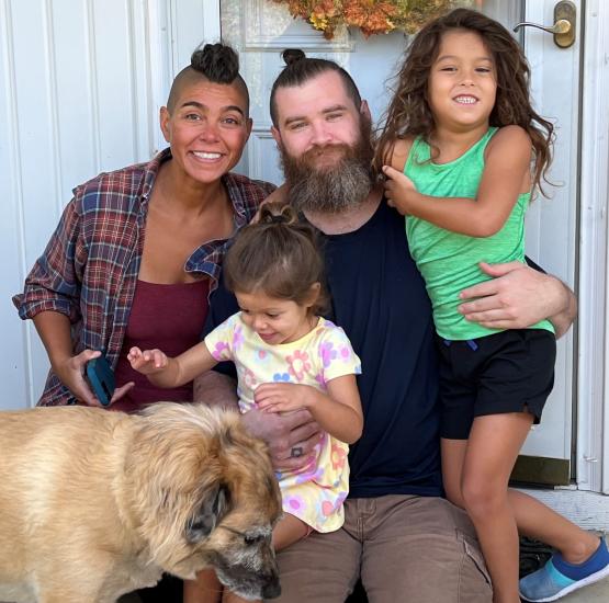 A photo of a family with a husband, wife, two young children and a dog