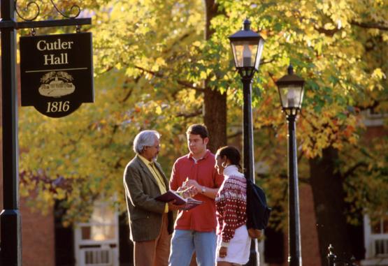 professor with two students near Cutler Hall sign on College Green with autumnal trees