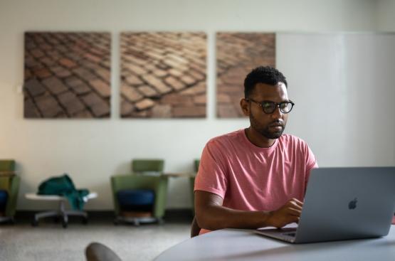 student sitting at a table on their laptop in a conference room
