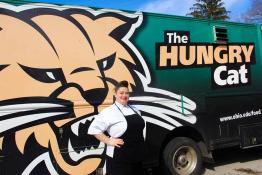 Dani poses in an apron and chef uniform in front of The Hungry Cat food truck.