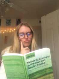 Taylor inquisitively reading a green copy of the second edition of the book, Threshold Concepts in Women’s and Gender Studies: Ways of Seeing, Thinking, and Knowing by Christie Launius and Holly Hassel. 