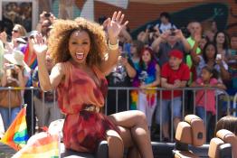 Janet Mock waving from the backseat of a convertible during a pride parade.